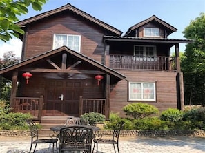 A two-story wooden house with a balcony, a front porch with a table and chairs, and red lanterns.