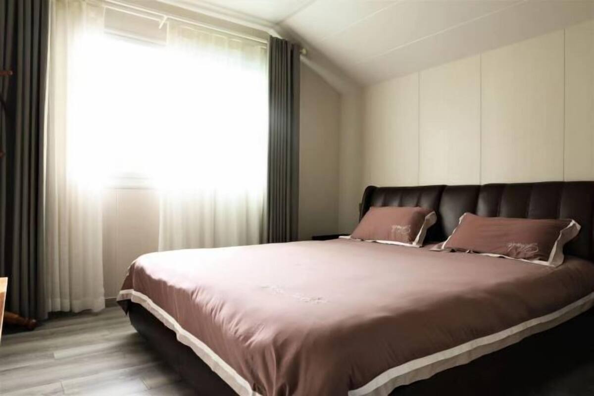 Un dormitorio con una cama grande, una ventana con cortinas y una pared de color claro.