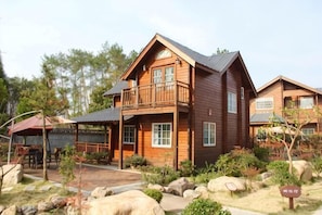 A wooden cabin with a balcony, a covered patio, and a landscaped garden with rocks and plants. - Tiantai Feitou Chalet (Tiantai County)