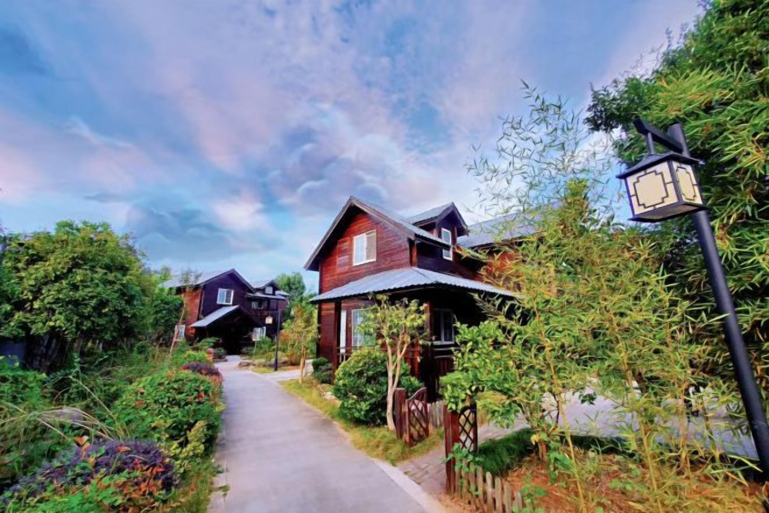 A pathway leading to a row of wooden houses with a street lamp on the right.