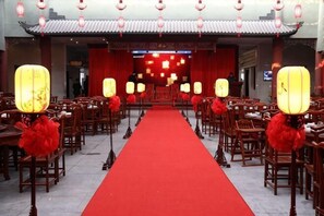 A traditional Chinese banquet hall with red carpets, wooden tables, and lanterns.
