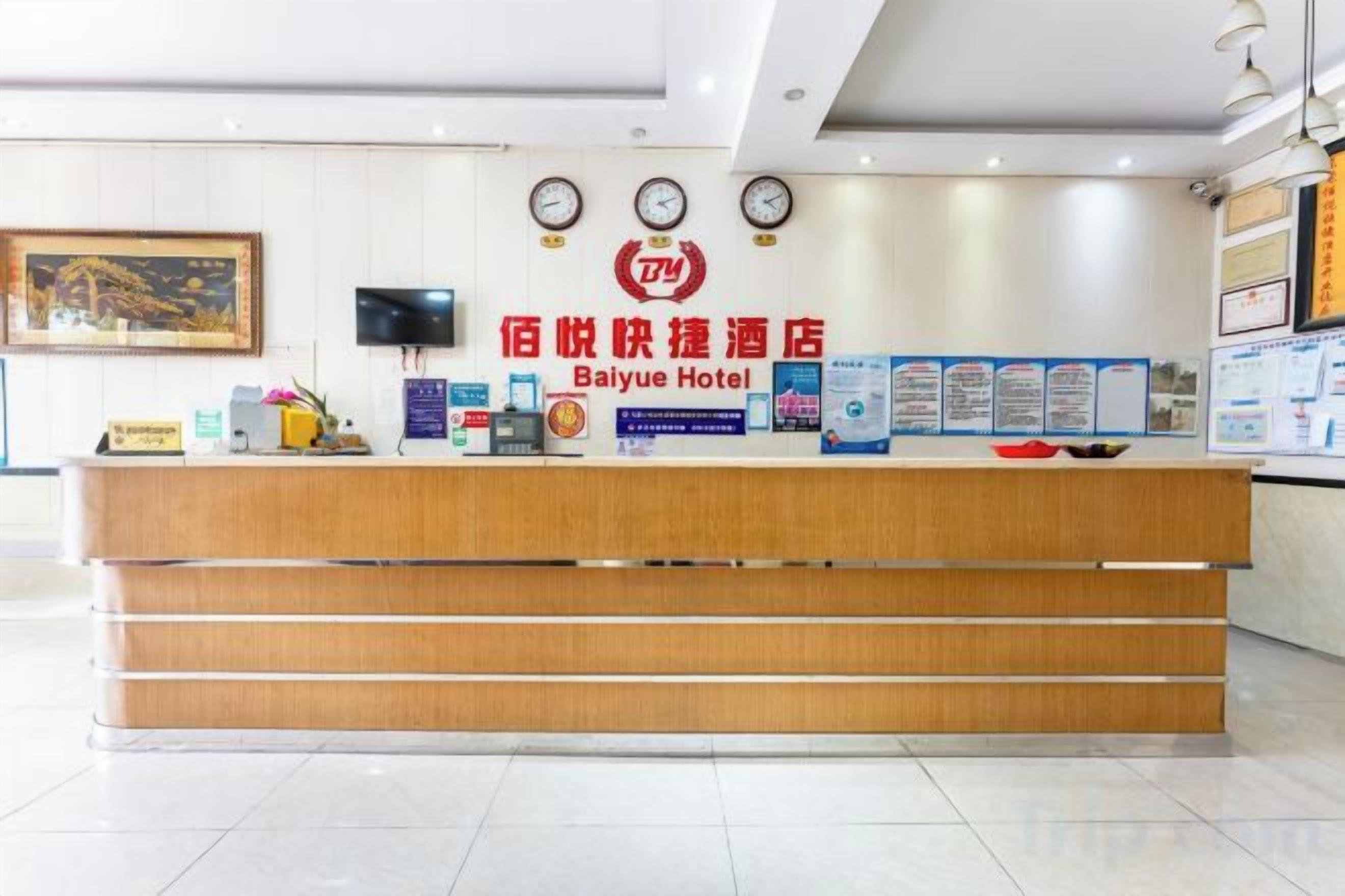 A hotel reception desk with a wooden counter, a clock, and informational posters on the wall.