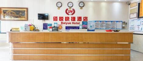 A hotel reception desk with a wooden counter, a clock, and informational posters on the wall.