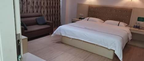 A hotel room with a bed, a nightstand, a lamp, a sofa, and a patterned wall.