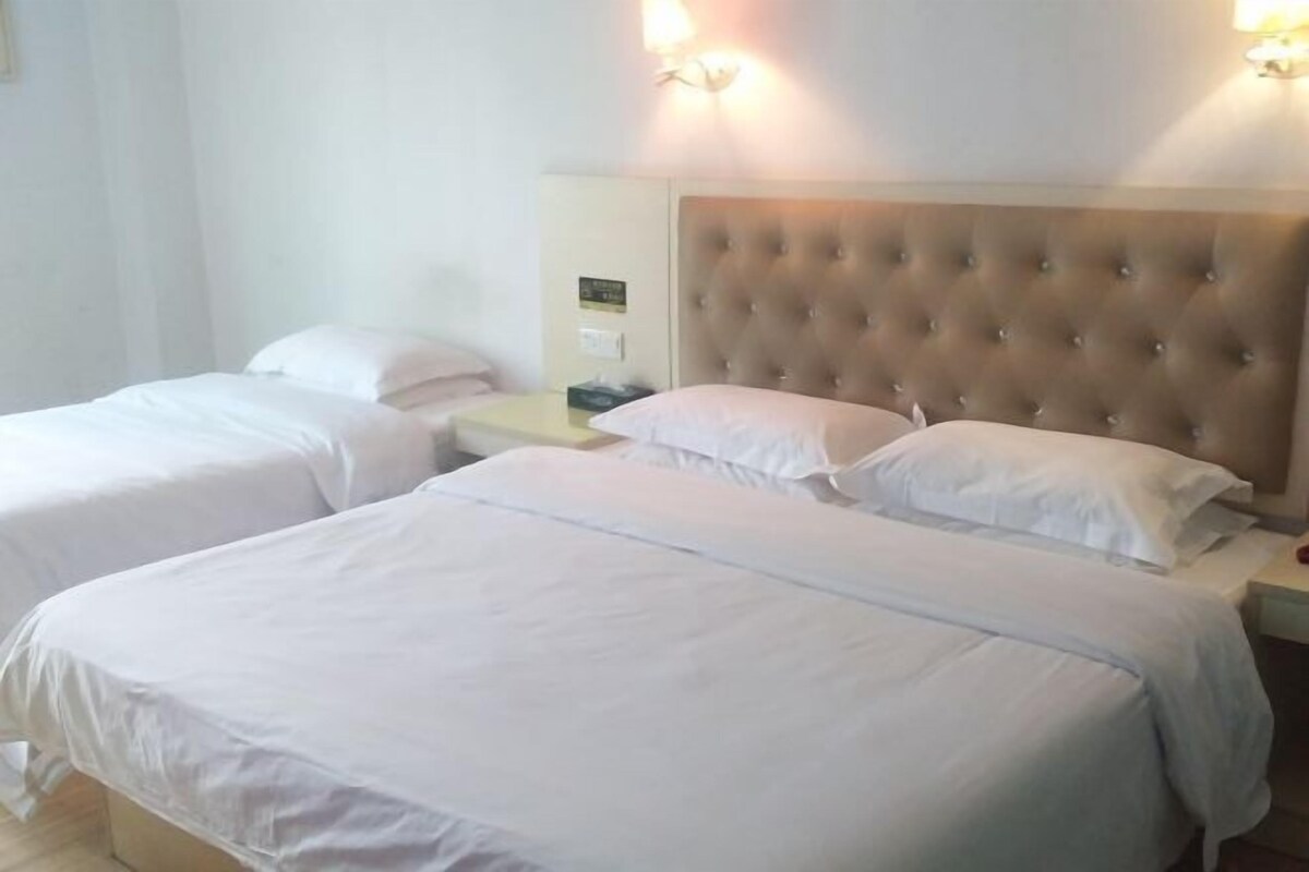 Habitación de hotel con dos camas, cada una con cabecero capitonado y ropa de cama blanca. Hay mesitas de noche con lámparas y un reloj pequeño.