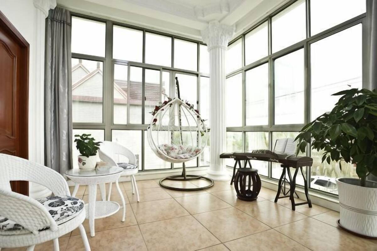 Una habitació àmplia amb grans finestres, una cadira penjant, mobles de vímet blanc i plantes en testos.