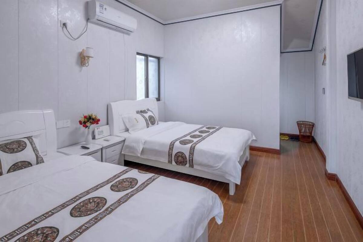 Una habitació d'hotel amb dos llits, una tauleta de nit, una taula petita amb un ram de flors i una finestra.