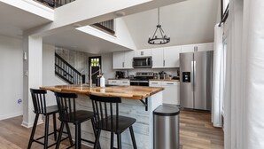 Eine moderne Küche mit einer Holztheke, schwarzen Barhocker, Edelstahlgeräten und einer Treppe zu einer oberen Ebene.