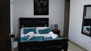 Un lit bien fait, avec une tête de lit, une table de chevet avec une lampe, un tableau encadré au mur et un miroir sur le mur.