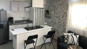 A modern kitchen with white cabinets, a gas stove, and a small island with two black chairs.