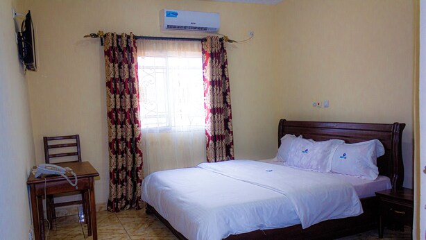 A bedroom with a bed, a chair, a desk, and an air conditioner. - DF Plazza Hotel (Yaoundé)