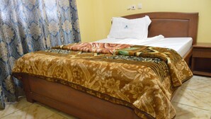 A bed with a patterned bedspread, a wooden headboard, and a white pillow. - DF Plazza Hotel (Yaoundé)