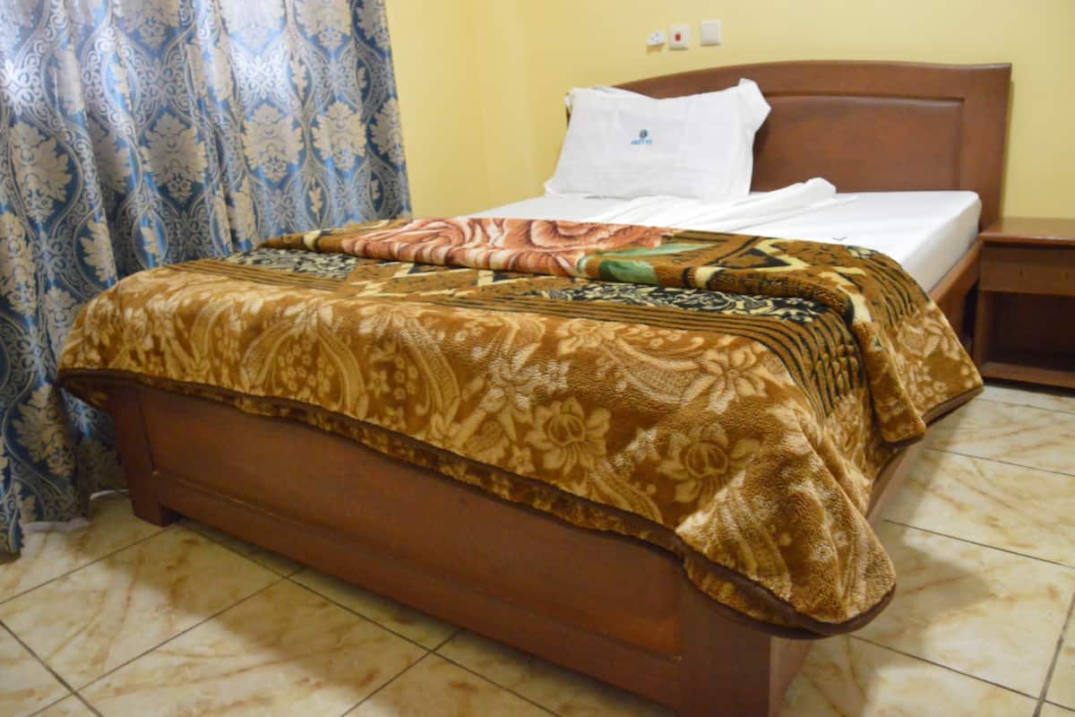 Una cama con colcha estampada, cabecero de madera y almohada blanca.