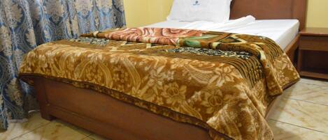 Una cama con colcha estampada, cabecero de madera y almohada blanca.