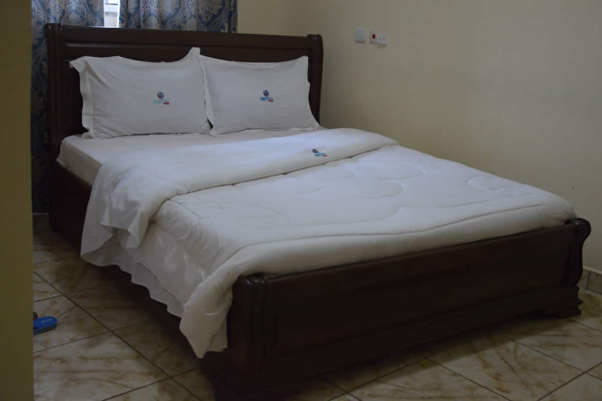 Una cama bien hecha con ropa blanca y almohadas, un cabecero de madera y piso de baldosas.