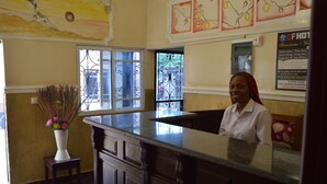 A reception area with a marble counter, a vase of flowers, and a signboard with room information. - DF Plazza Hotel (Yaoundé)