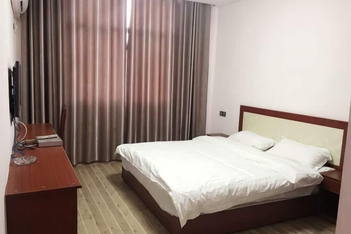 A hotel room with a bed, a desk, and a window with curtains.