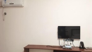 Une chambre dotée d’un téléviseur à écran plat fixé au mur, d’un bureau avec un ordinateur, d’une machine à café et d’une prise de courant.