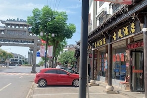 A street view with a red car parked on the side, a traditional building with a sign in a foreign language, and a bridge in the background. - Chibi Ancient Wind Hotel (Chibi)