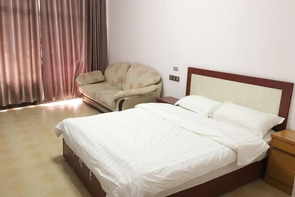 A hotel room with a bed, a nightstand, a chair, and a window with curtains.