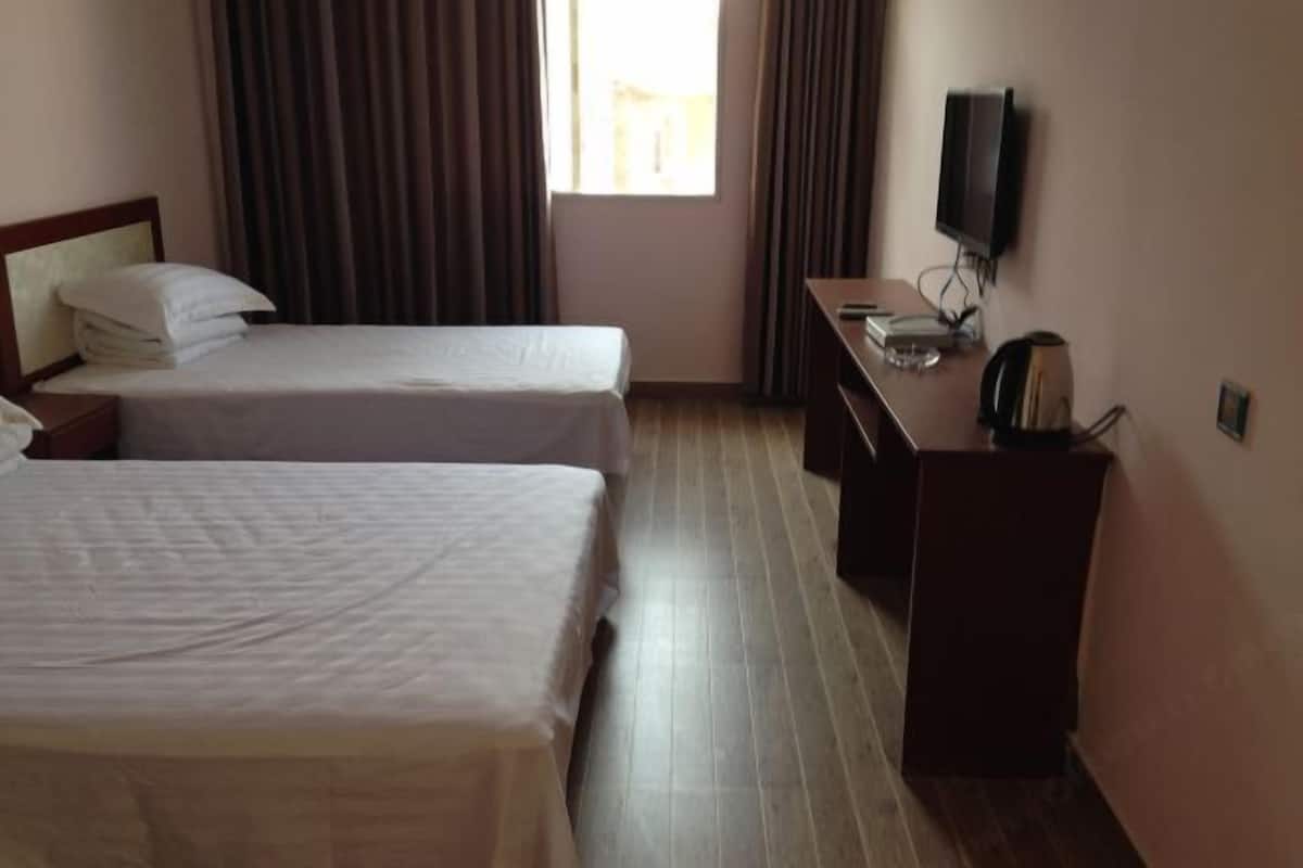 A hotel room with two beds, a desk with a television, and a window with curtains.