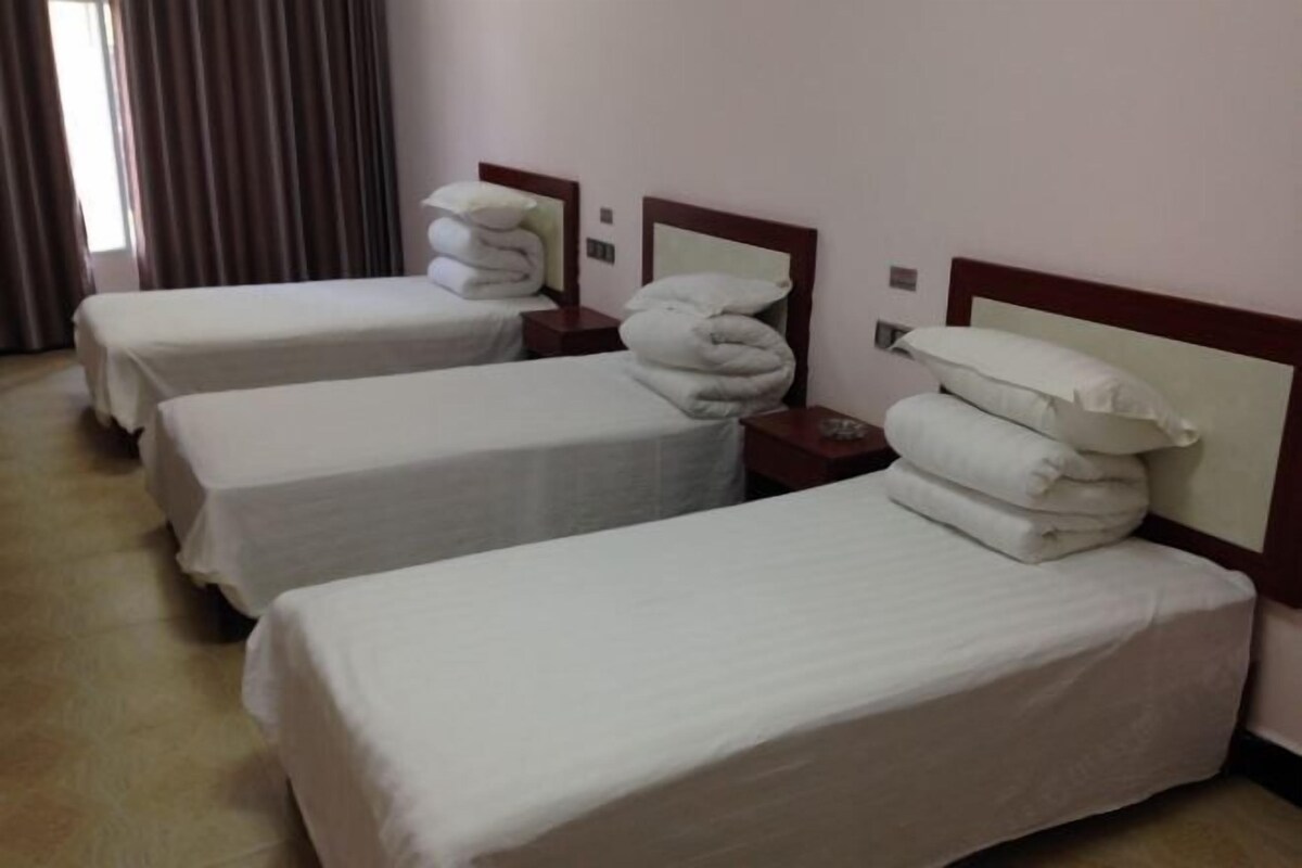 A hotel room with three single beds, each with white linens and pillows, and a wooden headboard.