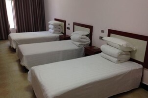 Habitación de hotel con tres camas individuales, cada una con ropa de cama y almohadas blancas, y cabeceros de madera.
