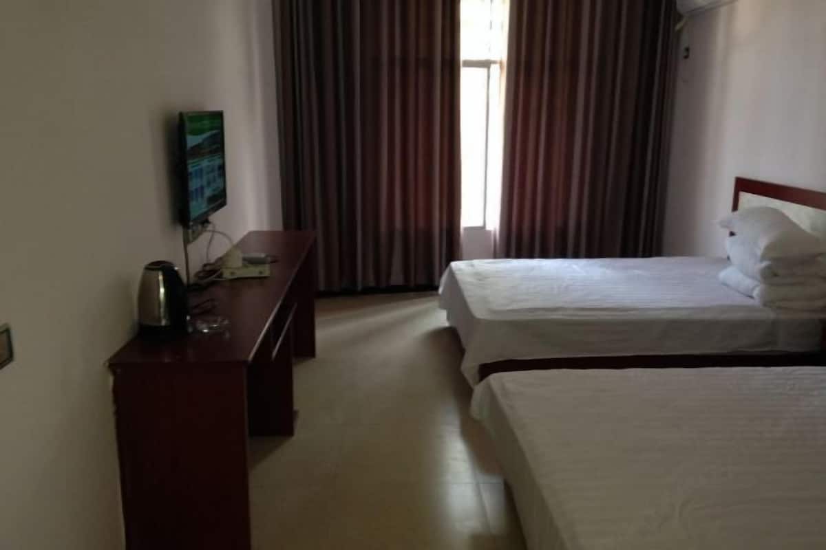 A hotel room with two beds, a desk with a television, and a window with curtains.