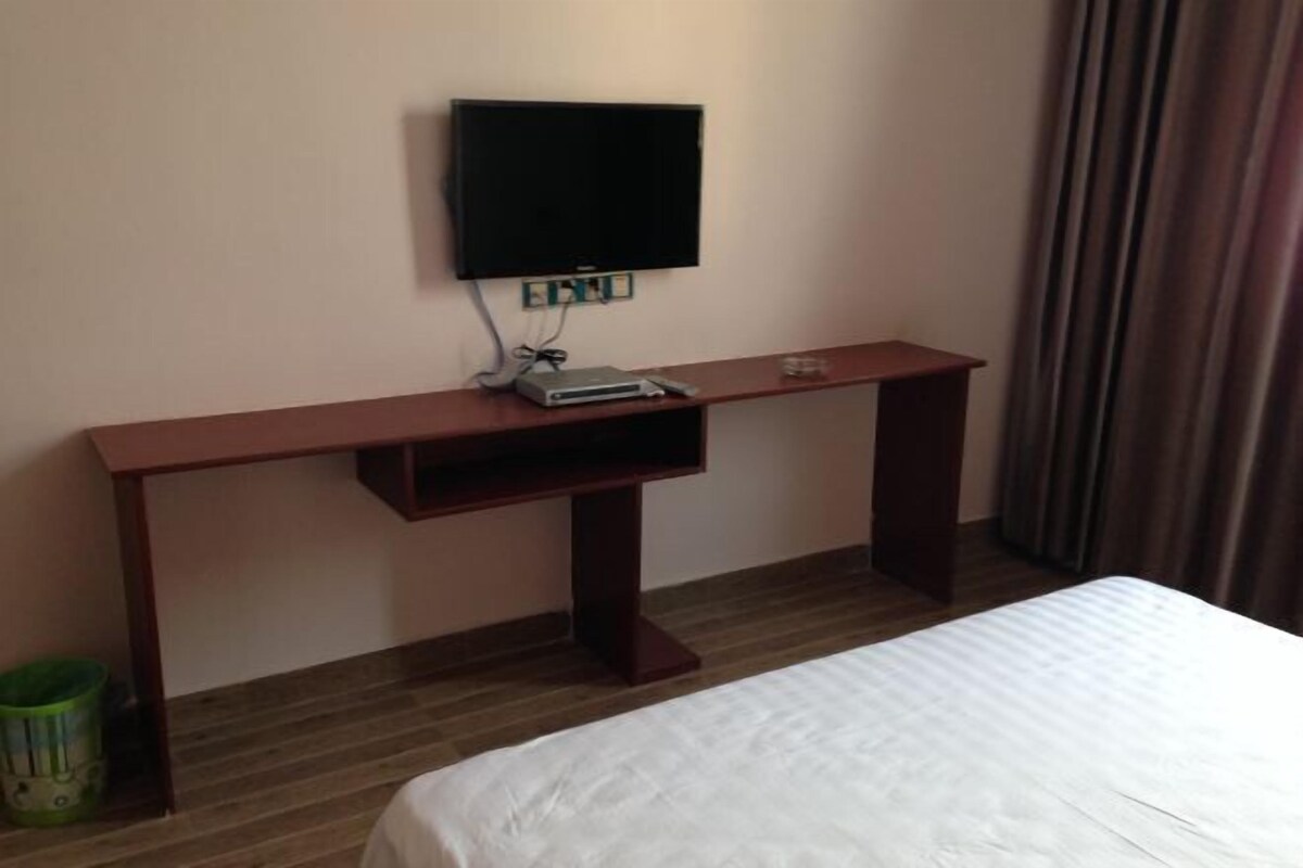 A hotel room with a bed, a TV mounted on the wall, a small table, and a trash bin.