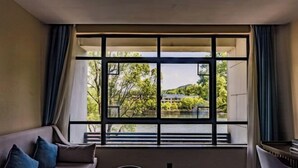 A room with a large window, a sofa, a round table, and a chair. - TONGXINLAKE HOTEL (You County)