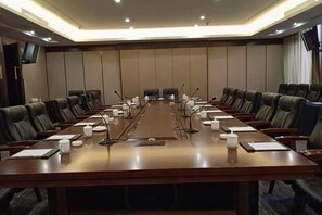A conference room with a long table, multiple chairs, microphones, and a television screen on the wall.