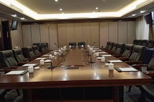 A conference room with a long table, multiple chairs, microphones, and a television screen on the wall.