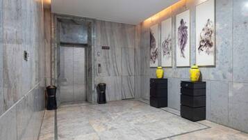 A hallway with a marble floor, a closed elevator, and artwork on the walls.