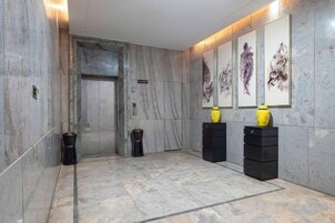 Un pasillo con piso de mármol, un ascensor cerrado y obras de arte en las paredes.