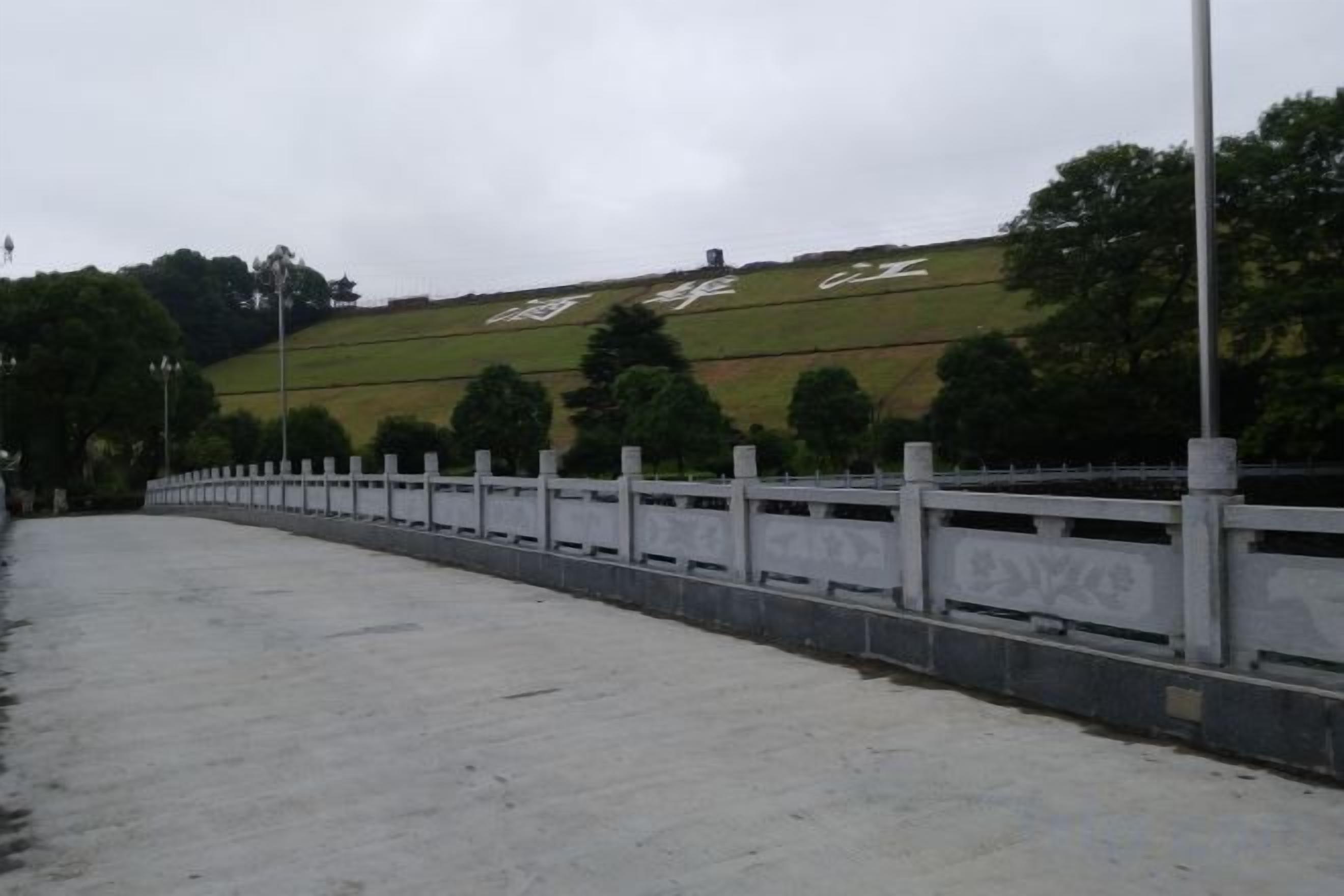 A paved pathway with a white fence, a grassy hill with text, and trees in the background.