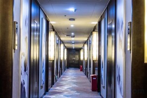 A hotel hallway with doors on both sides, a patterned carpet, and a red trash bin.