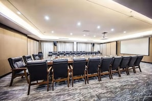 Une salle de conférence avec une longue table, des chaises, un écran de projection et un sol recouvert de moquette.