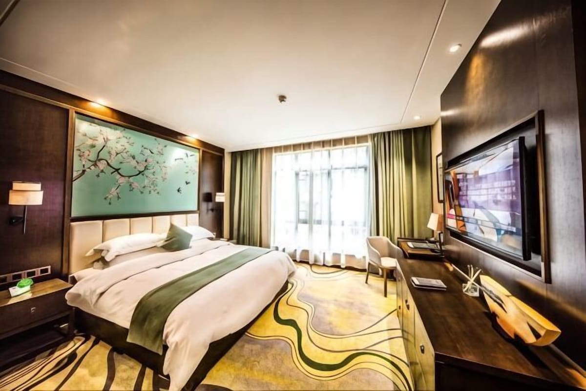 Une chambre d’hôtel avec un lit, une télévision, un bureau et une fenêtre avec des rideaux.
