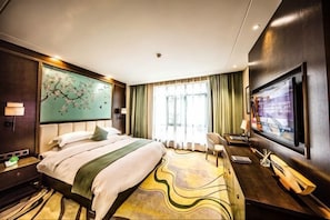 A hotel room with a bed, a TV, a desk, and a window with curtains.