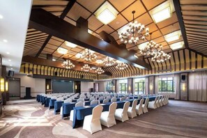 Une salle de conférence avec des rangées de tables et de chaises, un grand écran et un plafond haut doté d’une conception architecturale originale.