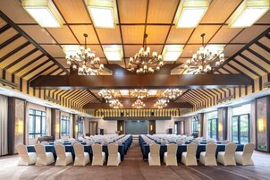 Un salón de conferencias con filas de sillas, una gran lámpara de araña y un techo alto con vigas de madera.