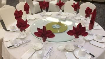 A round dining table with white chairs, each with a red napkin and glassware.