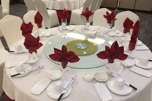 Una mesa redonda de comedor con sillas blancas, cada una con servilleta roja y cristalería.