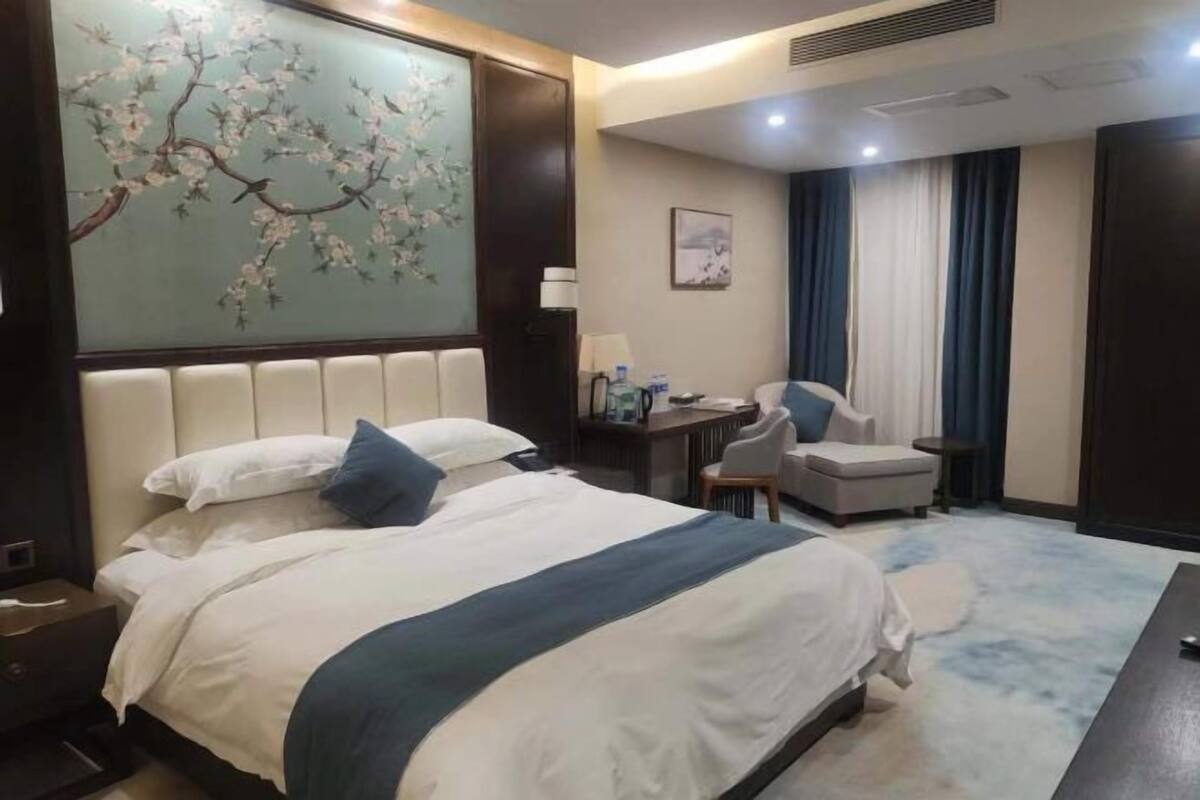 A hotel room with a large bed, a desk with a chair, a small table, and a painting on the wall.