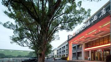 A hotel with a modern facade, a large tree in front, and a parking area with cars.
