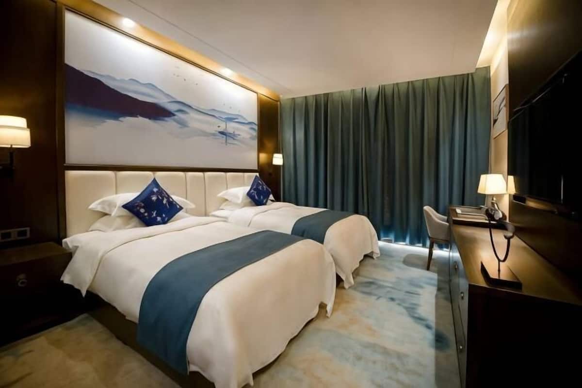 A hotel room with two beds, a desk, a TV, and a large painting on the wall.