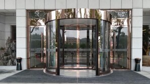 A revolving door entrance with glass panels and a metal frame, leading to a building with a stone facade and a tiled ground. - TONGXINLAKE HOTEL (You County)
