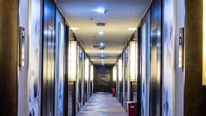 A hotel corridor with a patterned carpet, wall-mounted lights, and a red trash bin. - TONGXINLAKE HOTEL (You County)