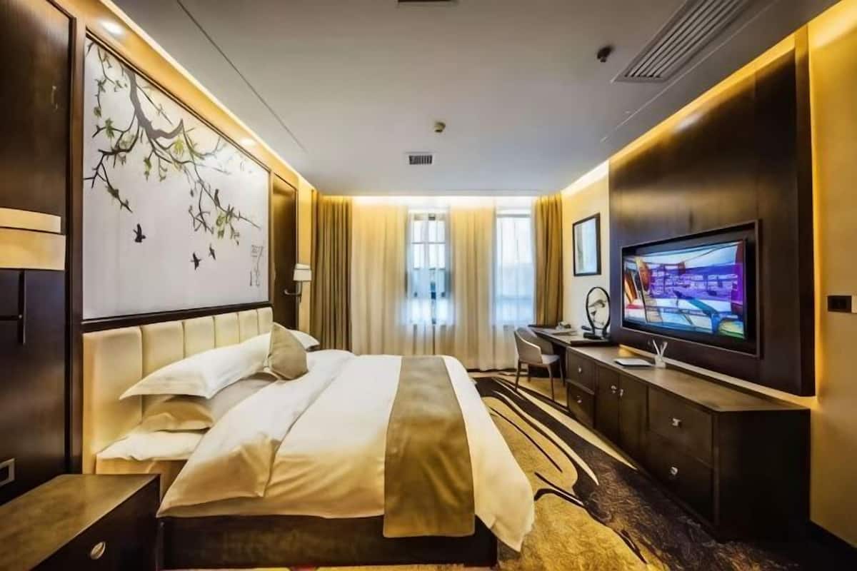 A hotel room with a bed, a desk, a television, and a large artwork on the wall.