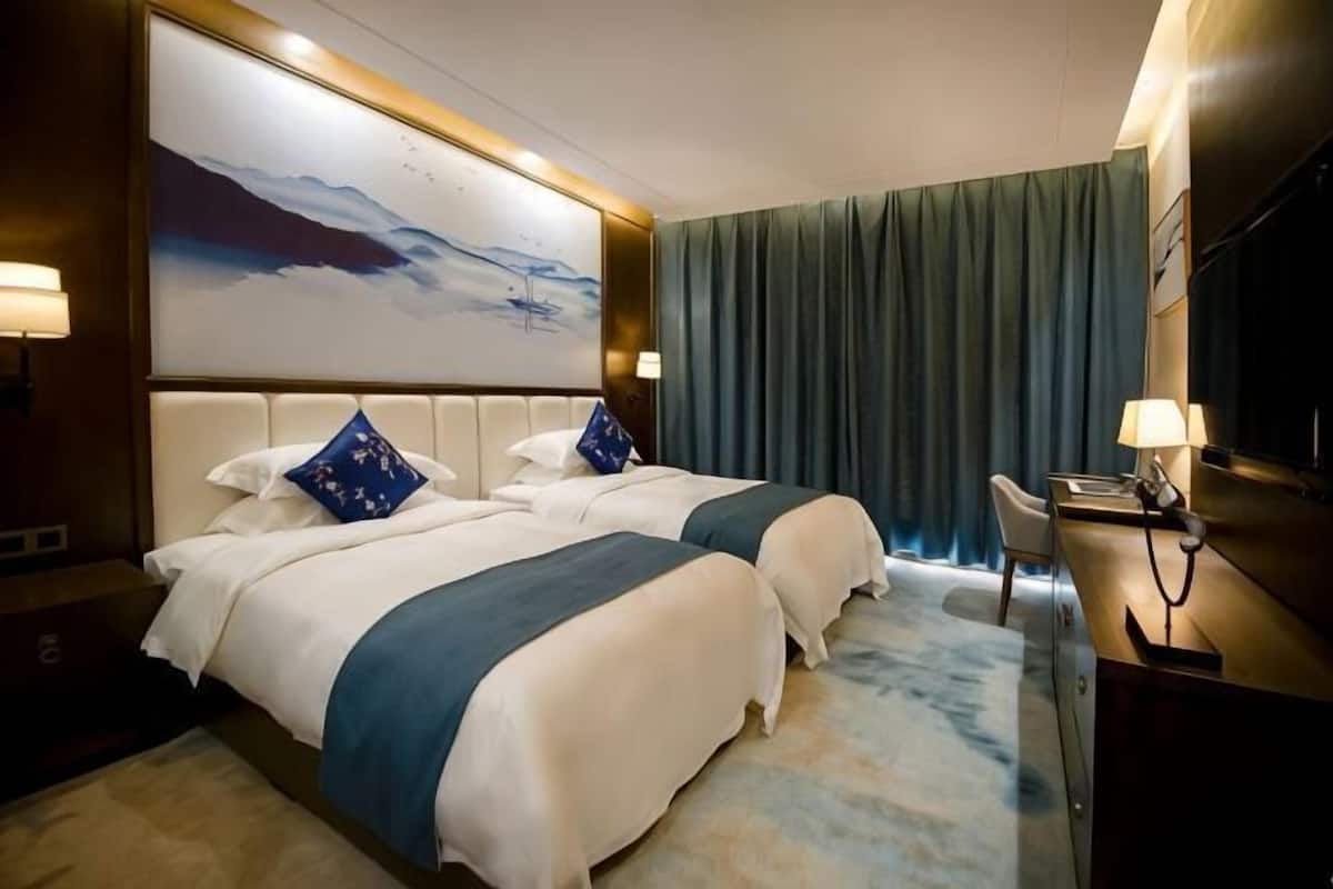 A hotel room with two beds, a large painting, a television, and a desk with a lamp.